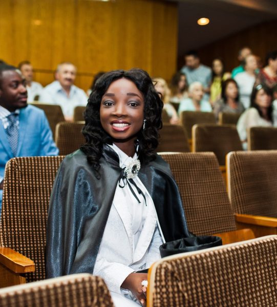 Happy beautiful black african american girl with hat and gown graduates at ceremony graduated